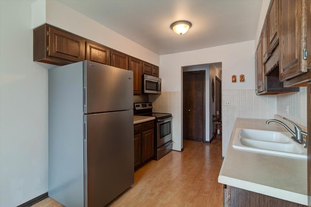 kitchen with tile walls, stainless steel appliances, light countertops, a sink, and light wood-type flooring