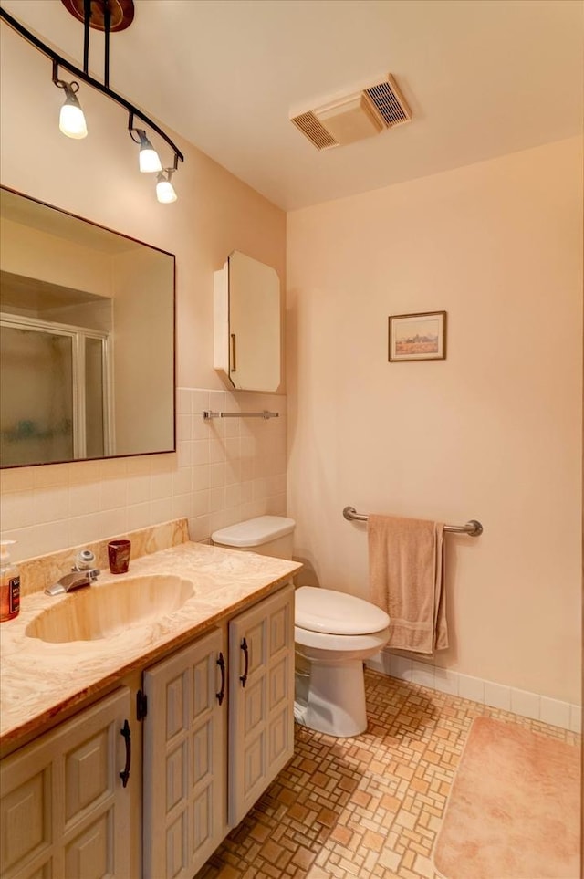 bathroom featuring visible vents, toilet, vanity, a shower stall, and tile walls