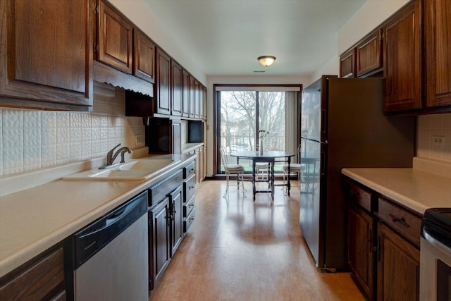 kitchen with stainless steel appliances, tasteful backsplash, light countertops, light wood-style floors, and a sink