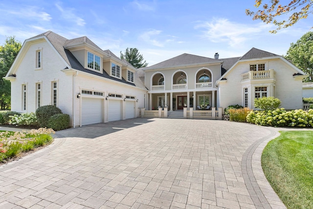 view of front of house featuring a garage, a balcony, a chimney, covered porch, and decorative driveway