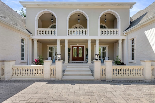 entrance to property with a porch, french doors, a balcony, and stucco siding