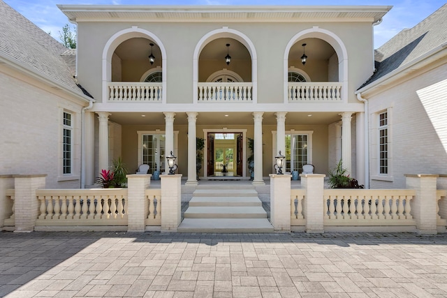 view of exterior entry featuring a balcony, stucco siding, and french doors