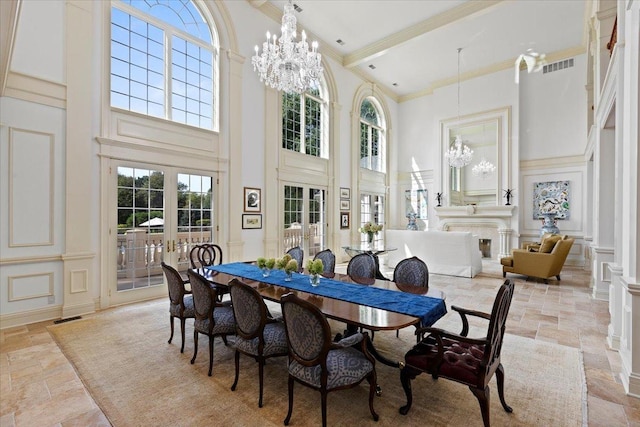 dining space featuring stone tile floors, an inviting chandelier, a high ceiling, crown molding, and a decorative wall