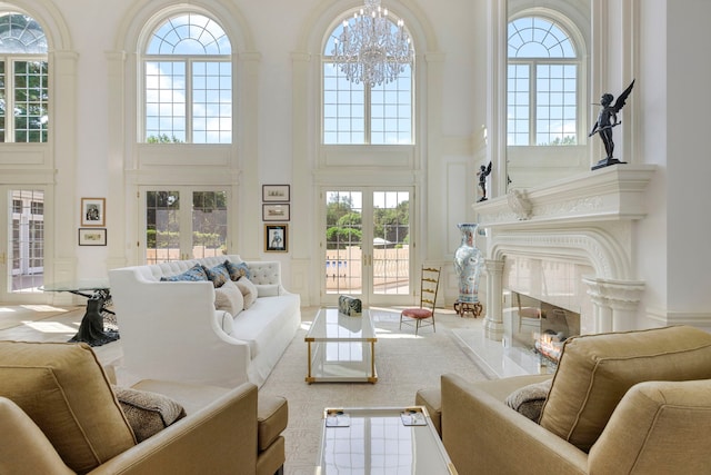 living area featuring a tile fireplace, a towering ceiling, french doors, a decorative wall, and a notable chandelier