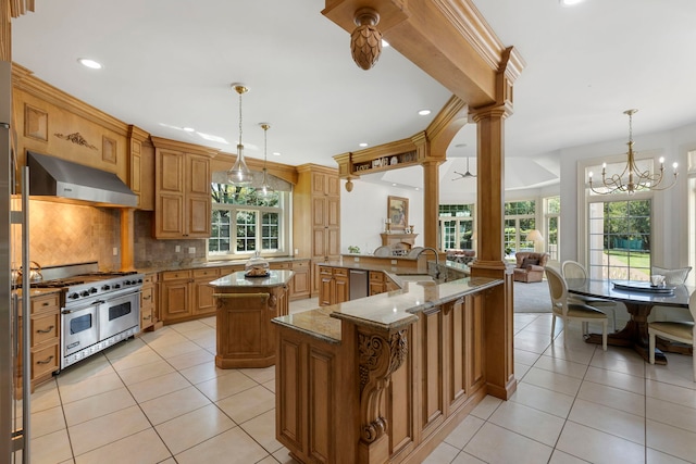 kitchen with under cabinet range hood, stainless steel appliances, a spacious island, a sink, and decorative columns