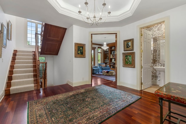 entrance foyer with a chandelier, a raised ceiling, ornamental molding, and wood finished floors