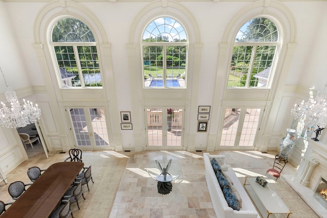 interior space with a high ceiling, a decorative wall, a notable chandelier, and french doors