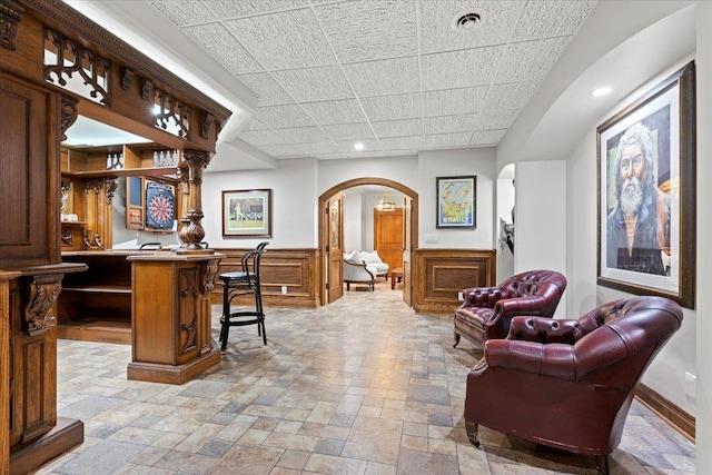 bar featuring arched walkways, indoor wet bar, a paneled ceiling, visible vents, and stone finish floor