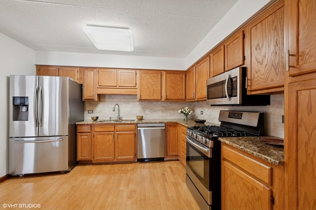 kitchen featuring appliances with stainless steel finishes, brown cabinetry, a sink, and light wood-style flooring