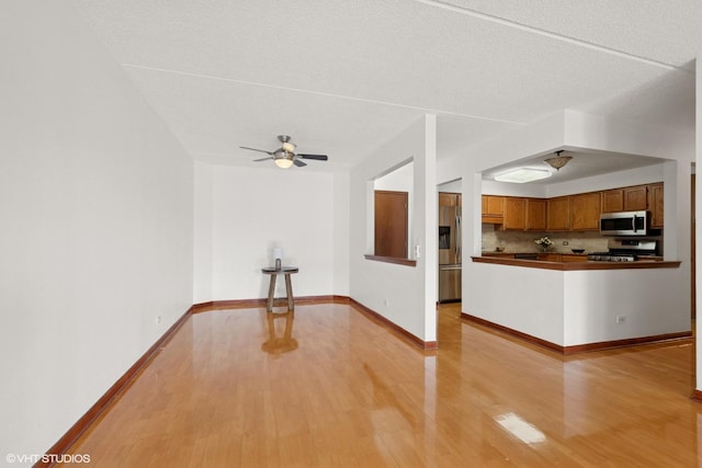 unfurnished living room featuring light wood finished floors, ceiling fan, baseboards, and a textured ceiling