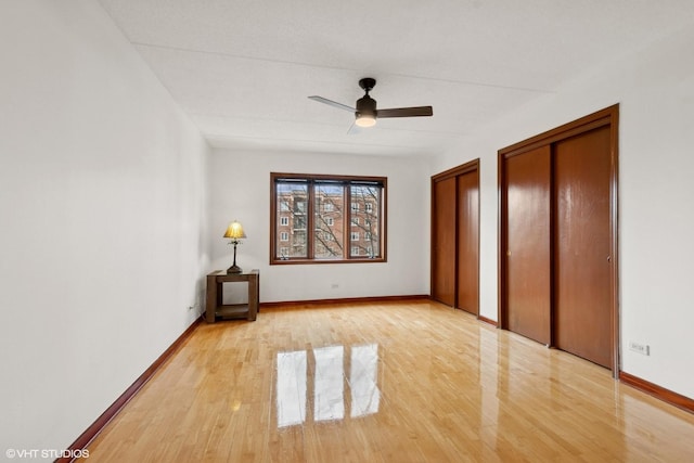 unfurnished bedroom featuring multiple closets, light wood-style flooring, and baseboards