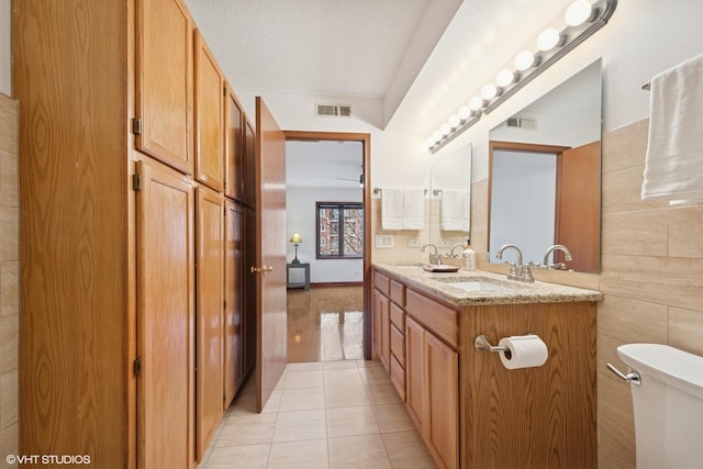 bathroom with tile patterned flooring, toilet, a sink, visible vents, and tile walls