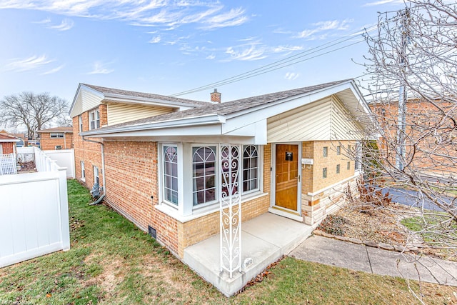 view of front facade featuring brick siding, fence, a chimney, and a front lawn