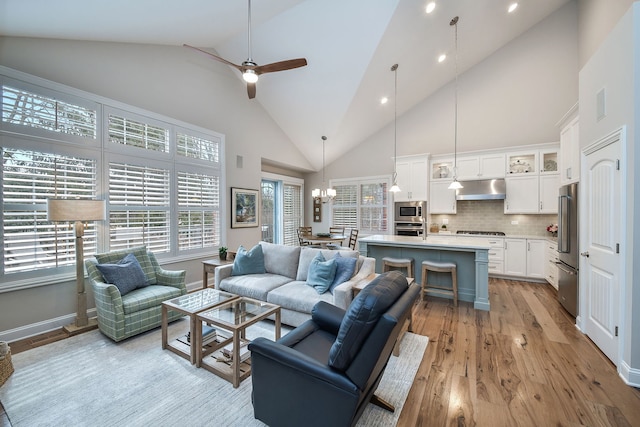 living area featuring ceiling fan with notable chandelier, high vaulted ceiling, a wealth of natural light, and light wood-style floors