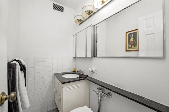 half bathroom with visible vents, tile walls, wainscoting, and vanity