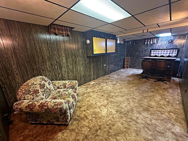 finished below grade area featuring carpet floors, wooden walls, a bar, and a paneled ceiling