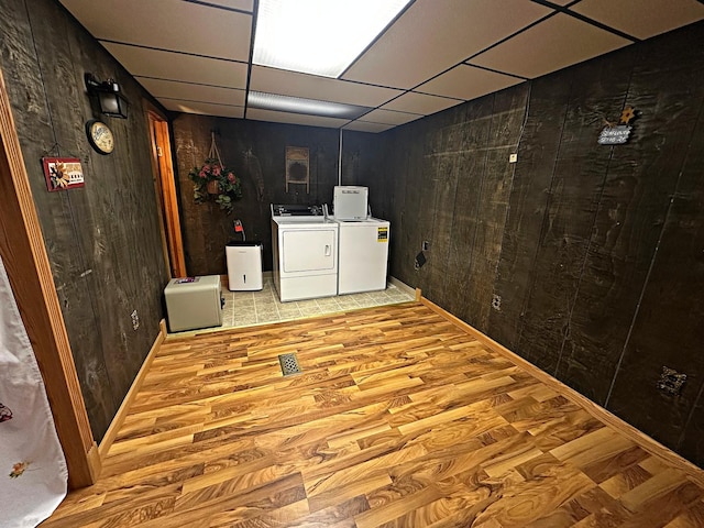 finished basement with light wood-style floors, a paneled ceiling, independent washer and dryer, and wooden walls