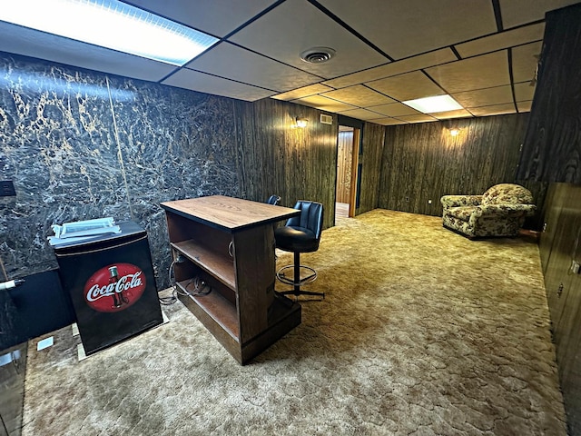 carpeted office space featuring wooden walls, visible vents, and a paneled ceiling