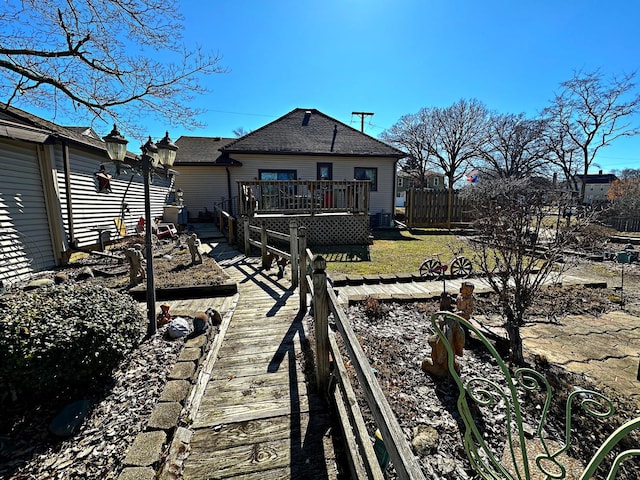 rear view of property featuring fence, a lawn, roof with shingles, a wooden deck, and a vegetable garden