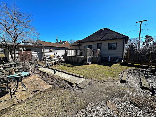 rear view of house with a wooden deck, a yard, fence, and roof with shingles