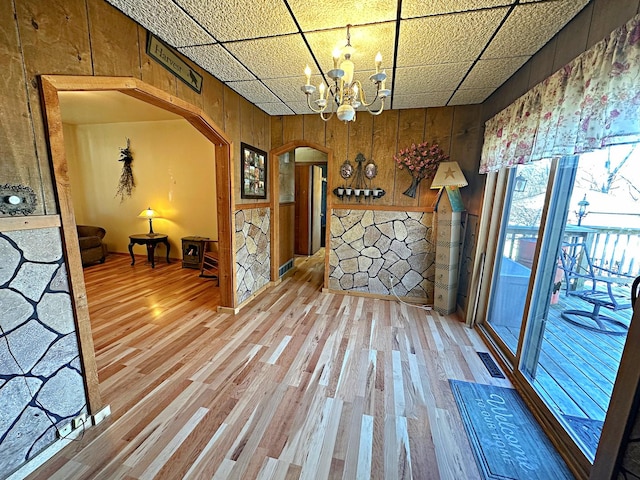 interior space with arched walkways, visible vents, light wood-style flooring, an inviting chandelier, and wood walls