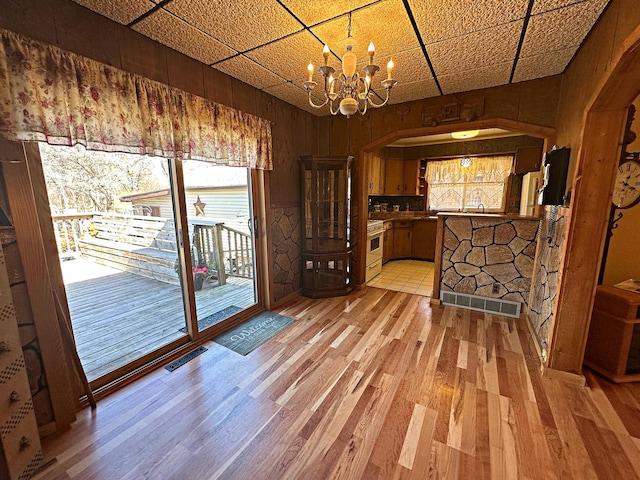 unfurnished dining area with a chandelier, arched walkways, visible vents, and light wood finished floors