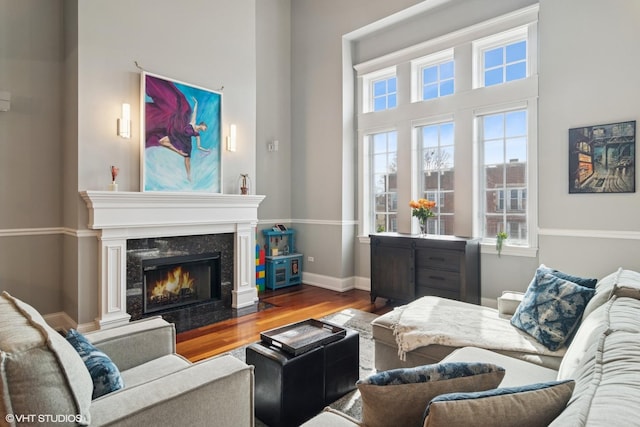 living area with a towering ceiling, a fireplace, baseboards, and wood finished floors