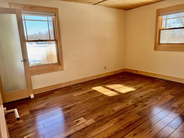 empty room featuring dark wood-type flooring, visible vents, and baseboards