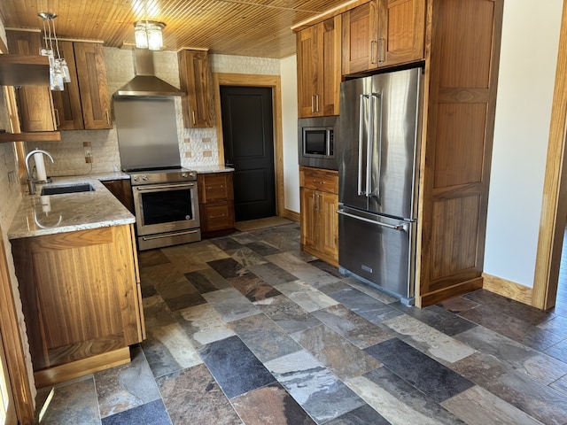 kitchen with stainless steel appliances, a sink, baseboards, wall chimney exhaust hood, and stone tile flooring