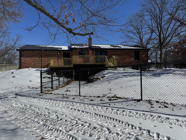 snow covered property featuring a deck, metal roof, brick siding, and a fenced front yard