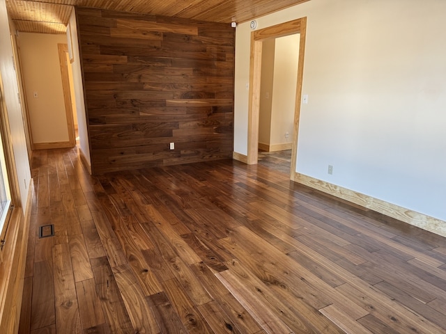 empty room with wood ceiling, wooden walls, baseboards, and dark wood-type flooring