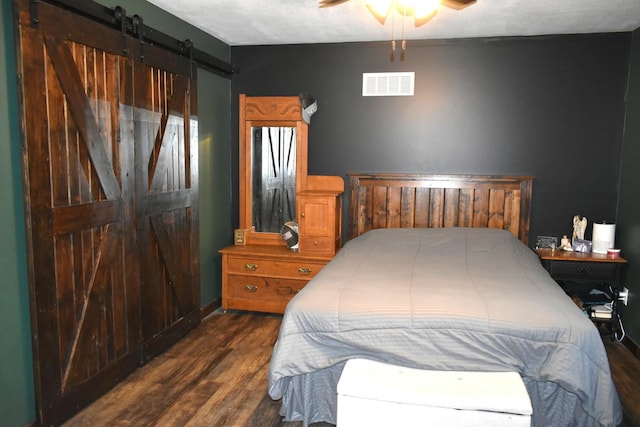 bedroom with a ceiling fan, a barn door, visible vents, and wood finished floors