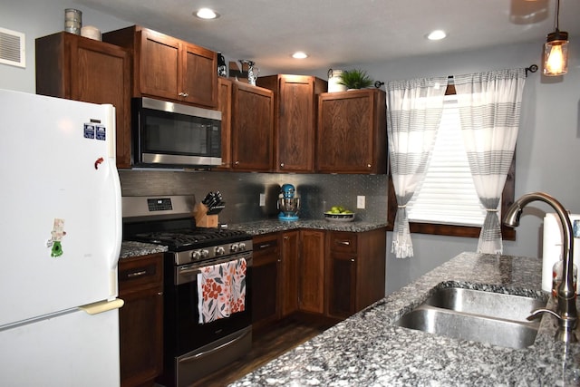 kitchen featuring stainless steel appliances, dark stone countertops, a sink, and decorative backsplash