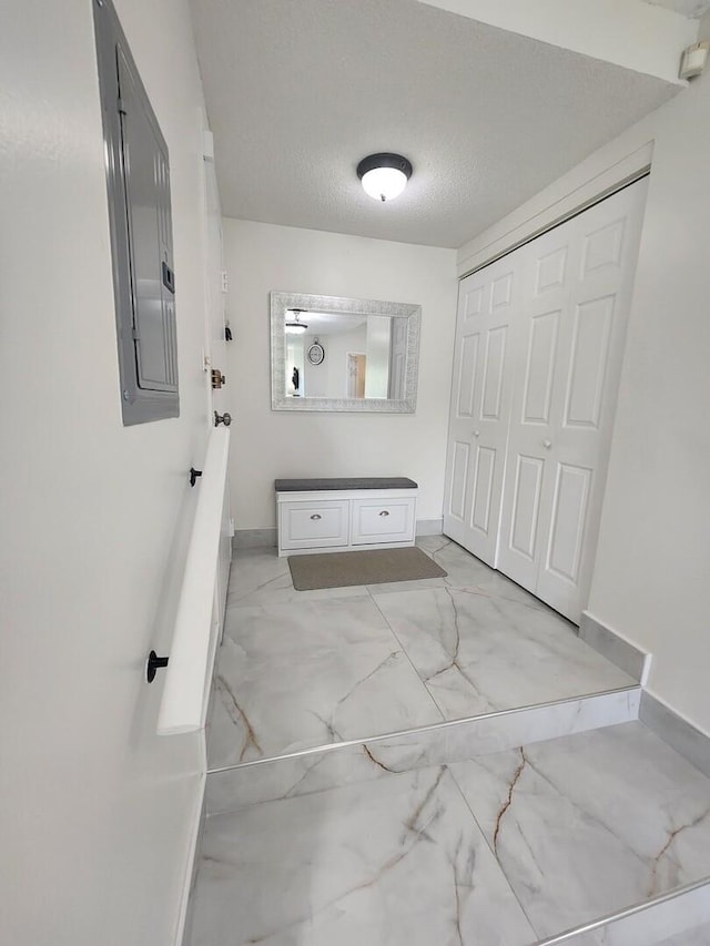 bathroom featuring a textured ceiling, marble finish floor, electric panel, and baseboards