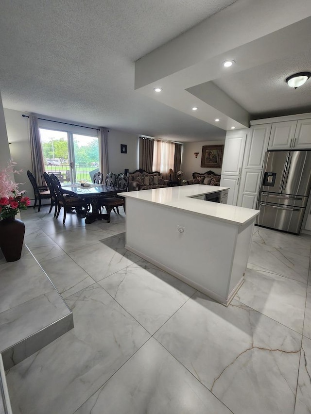 kitchen featuring stainless steel fridge, white cabinets, marble finish floor, light countertops, and a textured ceiling