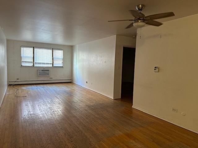 spare room featuring ceiling fan, a baseboard radiator, dark wood finished floors, and a wall mounted air conditioner