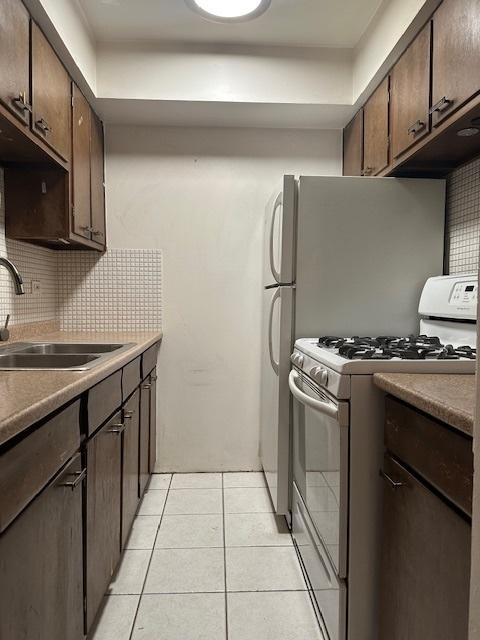 kitchen featuring dark brown cabinetry, white range with gas cooktop, light tile patterned floors, and a sink