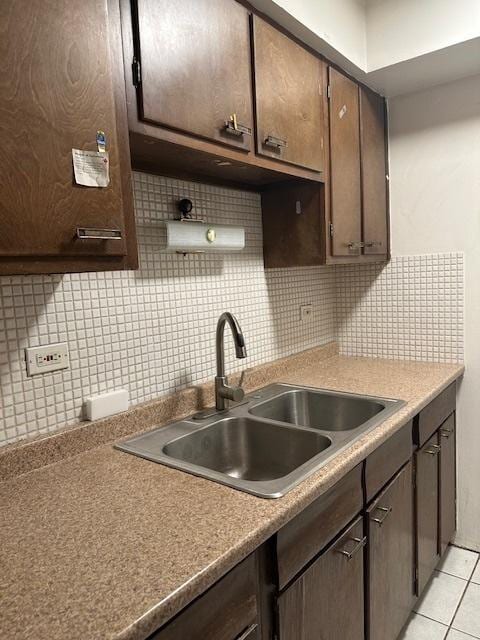 kitchen with tasteful backsplash, a sink, dark brown cabinetry, and light tile patterned floors