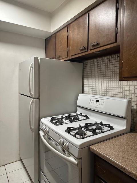 kitchen featuring light tile patterned floors, dark brown cabinets, backsplash, and white range with gas stovetop