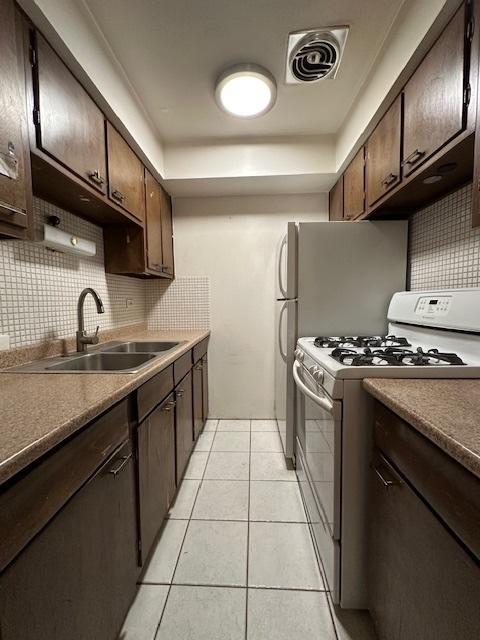 kitchen with light tile patterned floors, white gas range, visible vents, a sink, and dark brown cabinetry