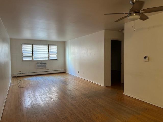 unfurnished room featuring a baseboard heating unit, a wall unit AC, ceiling fan, and dark wood-style floors