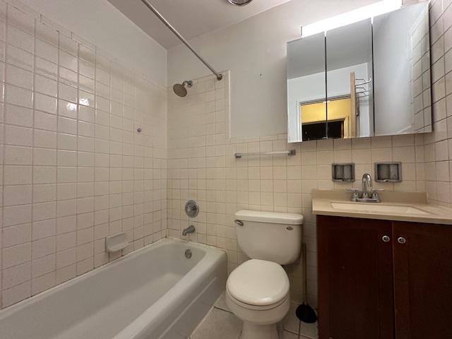 bathroom featuring toilet, tub / shower combination, tile walls, and vanity