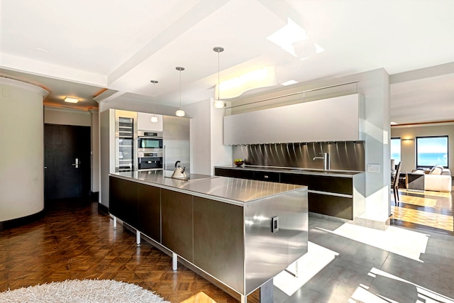 kitchen with a large island, modern cabinets, decorative light fixtures, stainless steel double oven, and stainless steel counters