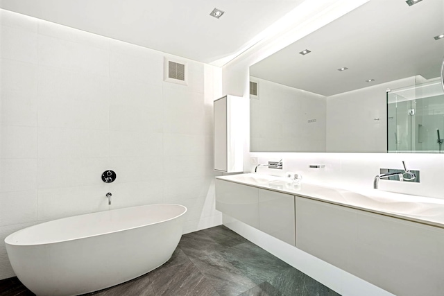 full bathroom with double vanity, a stall shower, visible vents, a freestanding tub, and tile walls