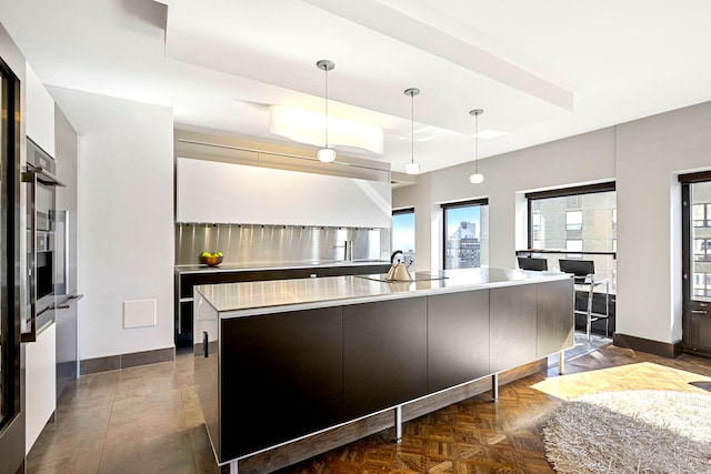 kitchen featuring a sink, light countertops, a tray ceiling, modern cabinets, and decorative light fixtures