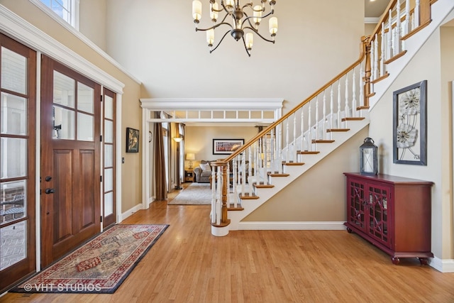 entryway featuring wood finished floors, stairway, a high ceiling, baseboards, and a chandelier