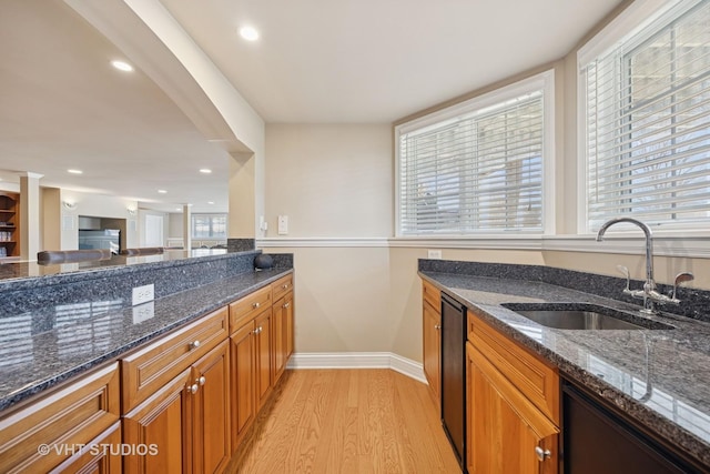 kitchen with brown cabinetry, dishwashing machine, light wood finished floors, and a sink