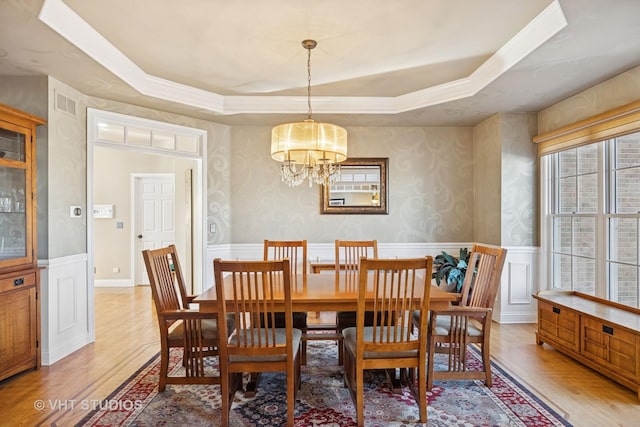 dining room featuring a chandelier, wainscoting, light wood-style flooring, and a raised ceiling