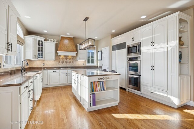 kitchen with white dishwasher, custom range hood, white cabinets, light wood-style floors, and a kitchen bar