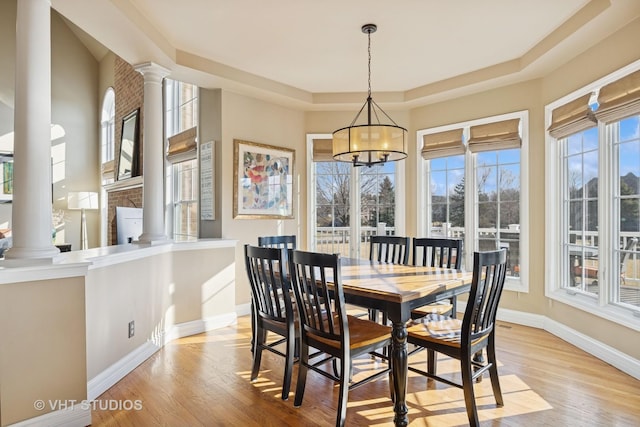 dining area with a tray ceiling, light wood-style floors, baseboards, and ornate columns